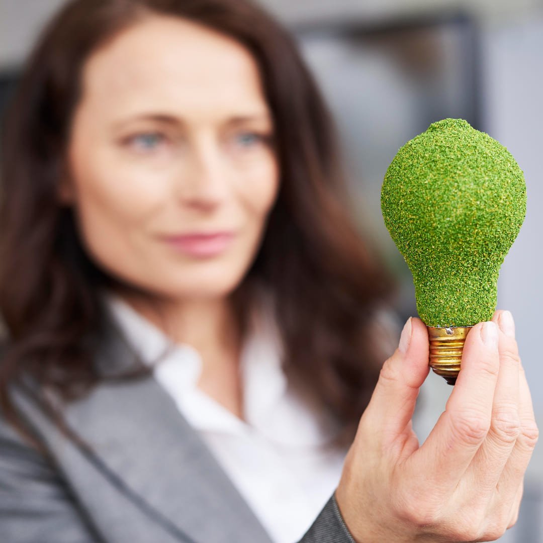 Vrouw met groene gloeilamp, symbool van milieubewustzijn. Zakelijke vrouw presenteert een duurzaam energie-idee. Concept: een helder groen idee voor de toekomst. Vrouw toont een innovatieve, eco-vriendelijke oplossing. Duurzaam denken: een groene gloeilamp in de hand.